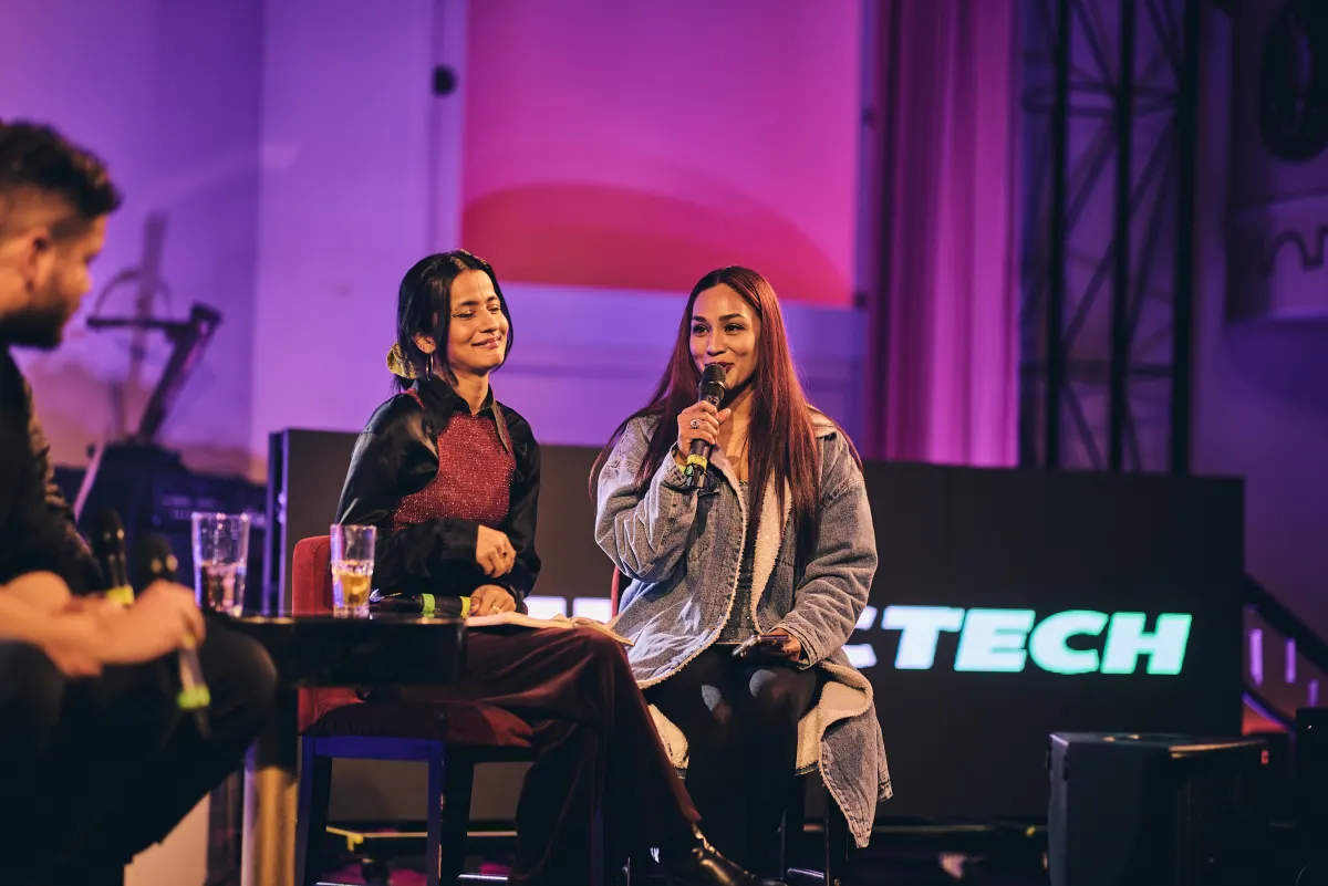 Two panellists on the purple-lit #MusicTech Slush 2024 stage, one speaking into a microphone while the other smiles