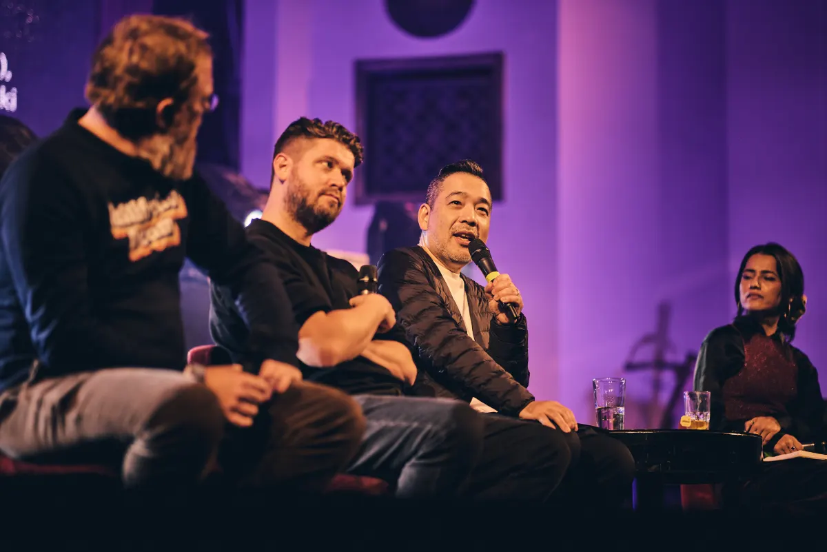Four people on the purple-lit #MusicTech Slush 2024 stage, the panellist in a quilted jacket speaking into a microphone as the others listen