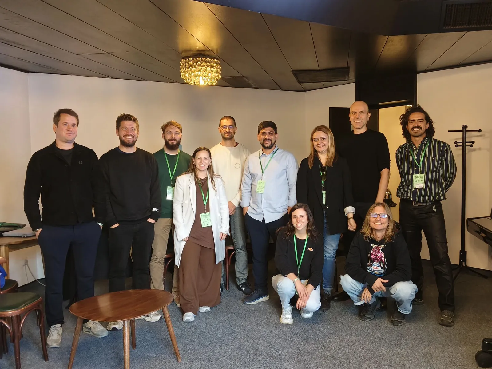Twelve people wearing green SoAlive lanyards pose together in a white-walled room in Sofia, ten standing and two crouching at the front