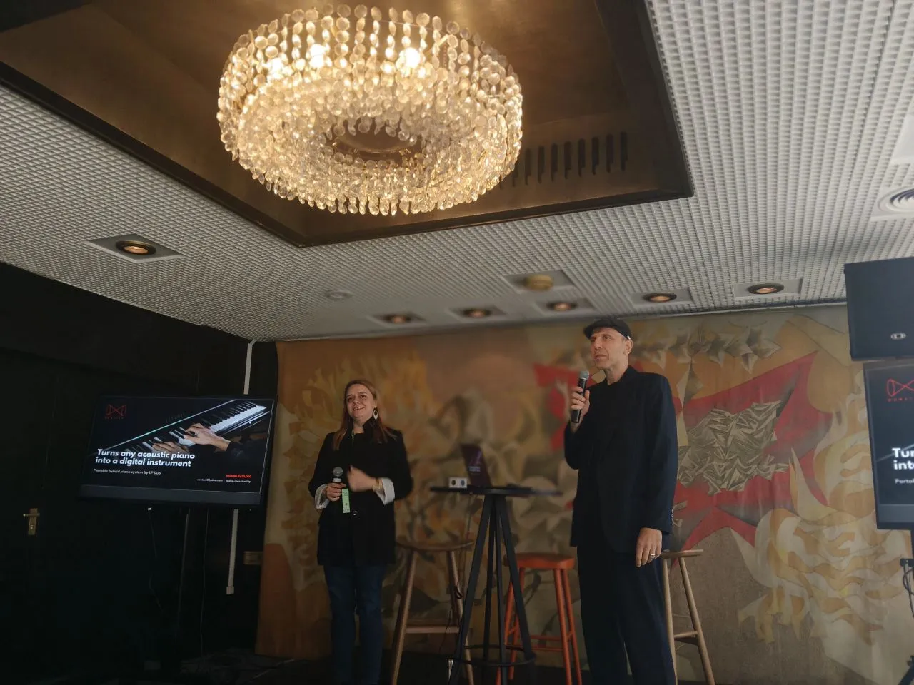 Two presenters with microphones pitch LP Duo on the SoAlive stage in Sofia, beside a screen reading 'Turns any acoustic piano into a digital instrument'